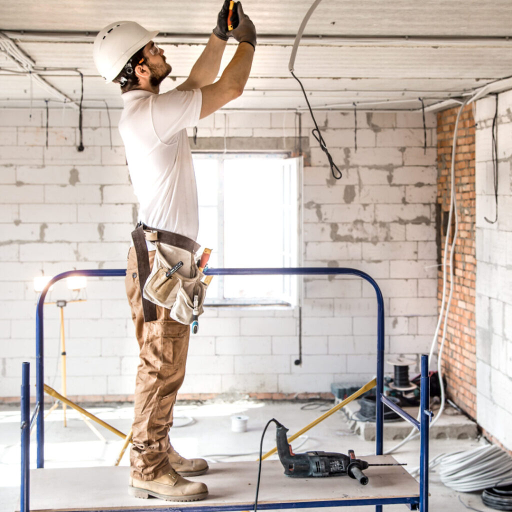 Electrician installer with a tool in his hands, working with cable on the construction site.